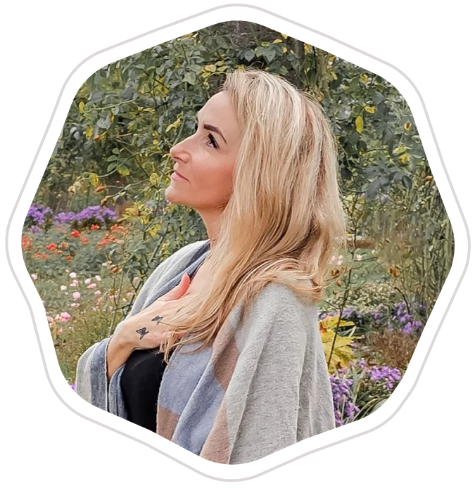 Frau mit langen blonden Haaren, die im Freien steht und nachdenklich in die Ferne blickt.